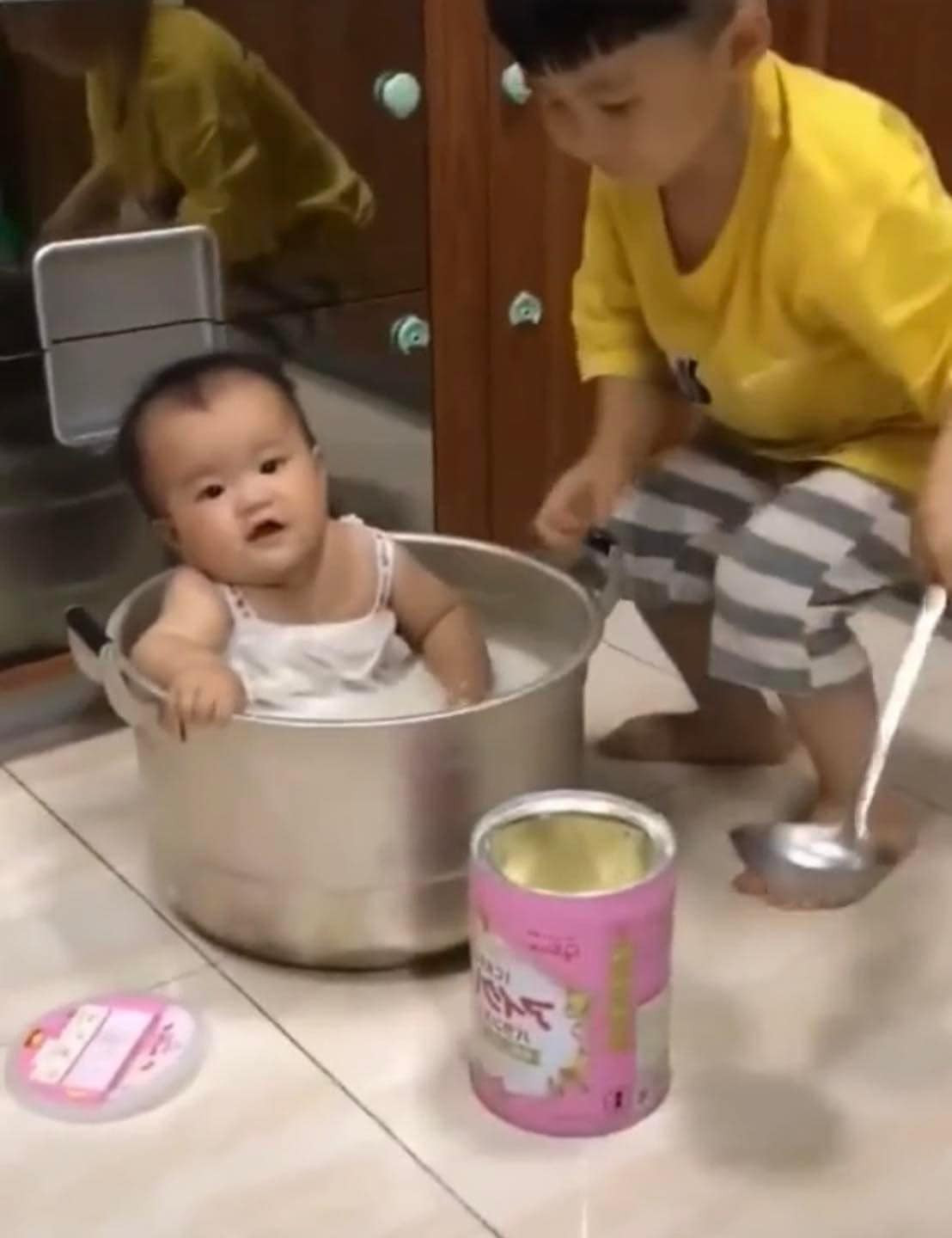 Chiếc nồi là bồn tắm, sữa bột là xà phòng tắm, trông mặt em bé còn có vẻ thích thú.