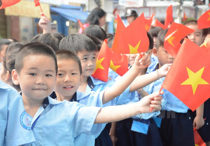 Các em học sinh nhỏ trên tay cờ hoa tươi vui trong ngày khai giảng.