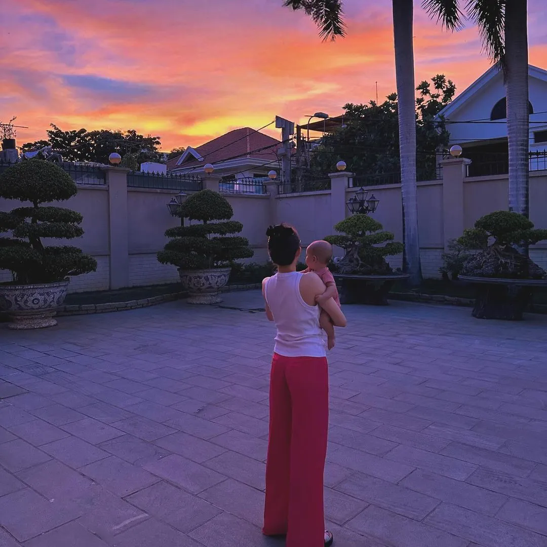 Trong ảnh, nàng dâu hào môn bế con đứng trong sân nhà ngắm hoàng hôn.