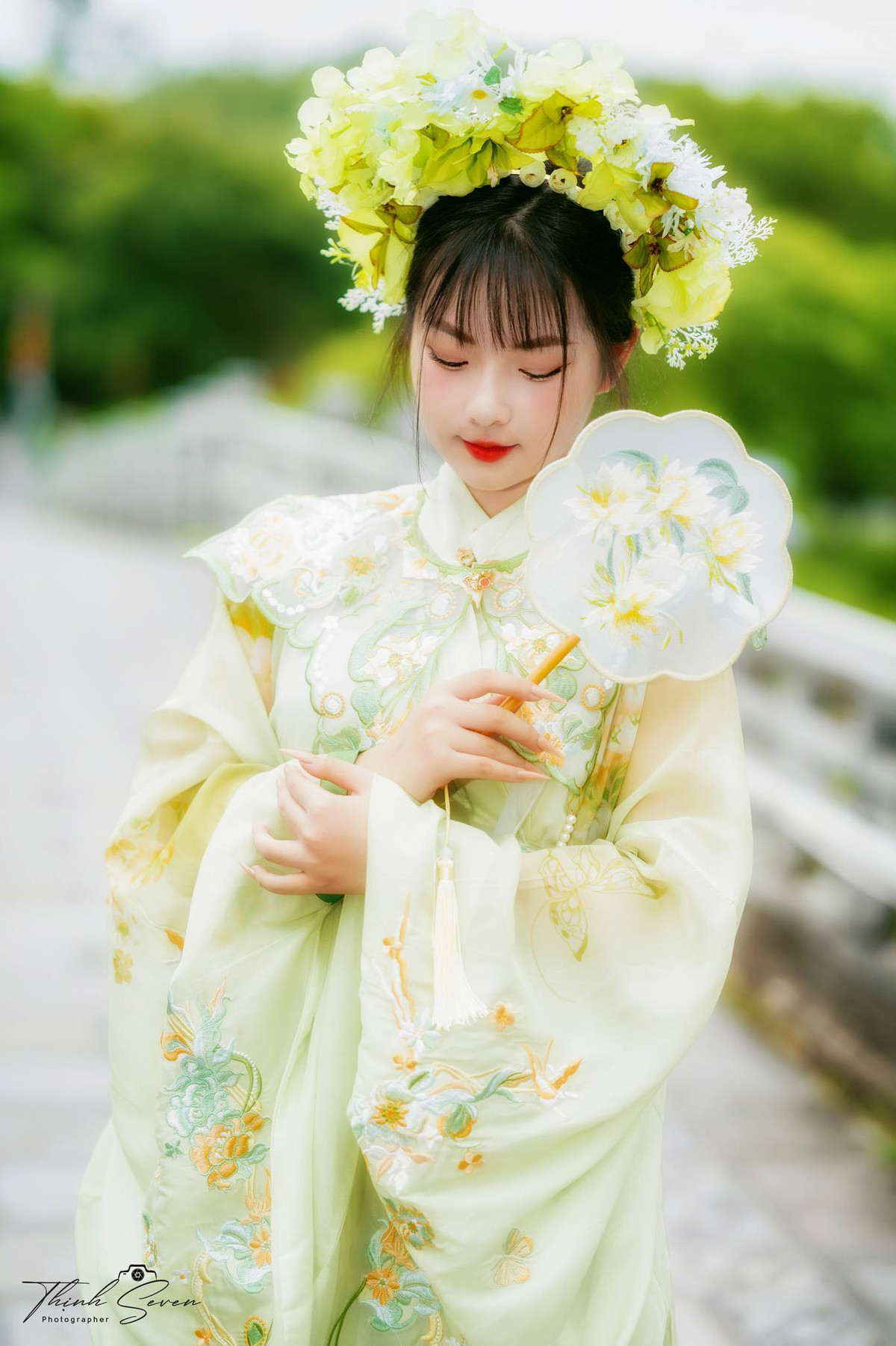 Tóc được khéo léo buộc ra sau đầu, cài một chiếc kẹp tóc màu ngà, đội một vòng hoa hoặc nụ hoa, cài thêm vài vòng hoa lụa hoặc hoa tươi, cuối cùng dùng kẹp tóc hoặc lược vàng, bạc để cố định kiểu tóc. (Ảnh: Thịnh Seven)