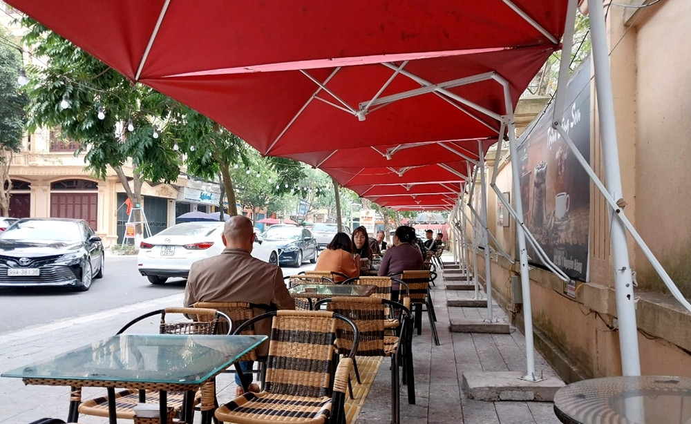 Các hộ dân kinh doanh đua nhau lấn chiếm vỉa hè, dựng ô dù, kèm với đó là bàn ghế bày tràn lan, dán biển quảng cáo, xếp đặt chậu cây cảnh để phục vụ buôn bán.