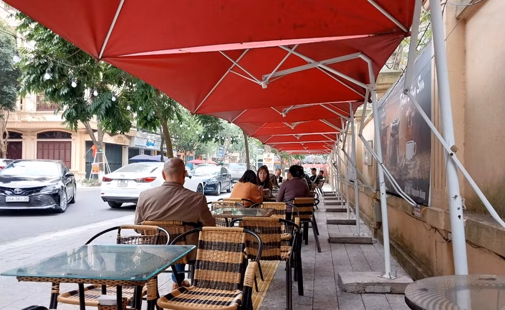 Các hộ dân kinh doanh đua nhau lấn chiếm vỉa hè, dựng ô dù, kèm với đó là bàn ghế bày tràn lan, dán biển quảng cáo, xếp đặt chậu cây cảnh để phục vụ buôn bán.