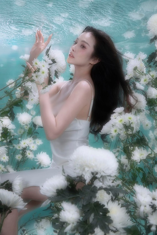 Nữ diễn viên diện chiếc váy hai dây trễ nải khoe vòng một, tạo dáng giữa những bông hoa trắng.