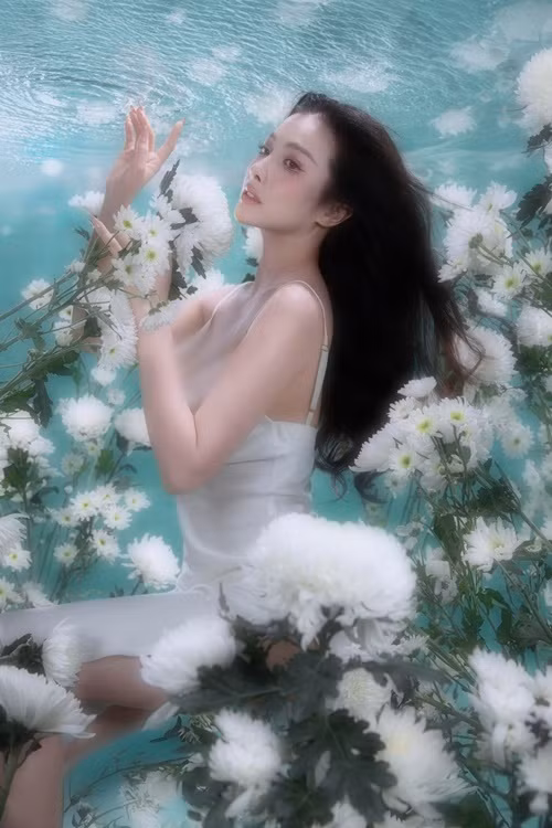 Nữ diễn viên diện chiếc váy hai dây trễ nải khoe vòng một, tạo dáng giữa những bông hoa trắng.