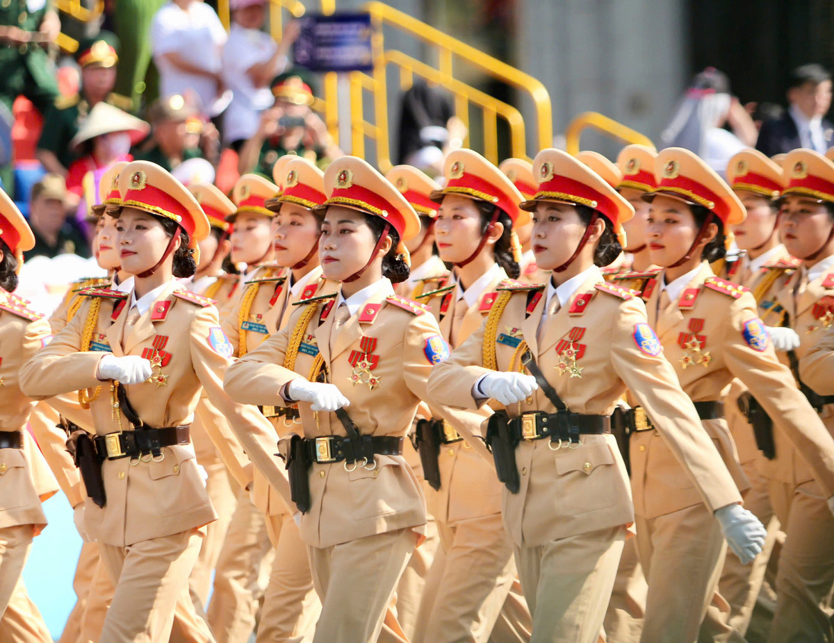 Khối nữ cảnh sát giao thông mặc lễ phục vàng kem đặc trưng, đội mũ kê-pi viền đỏ, mang găng tay trắng và thắt lưng da nâu, diễu hành trang nghiêm và đồng bộ.