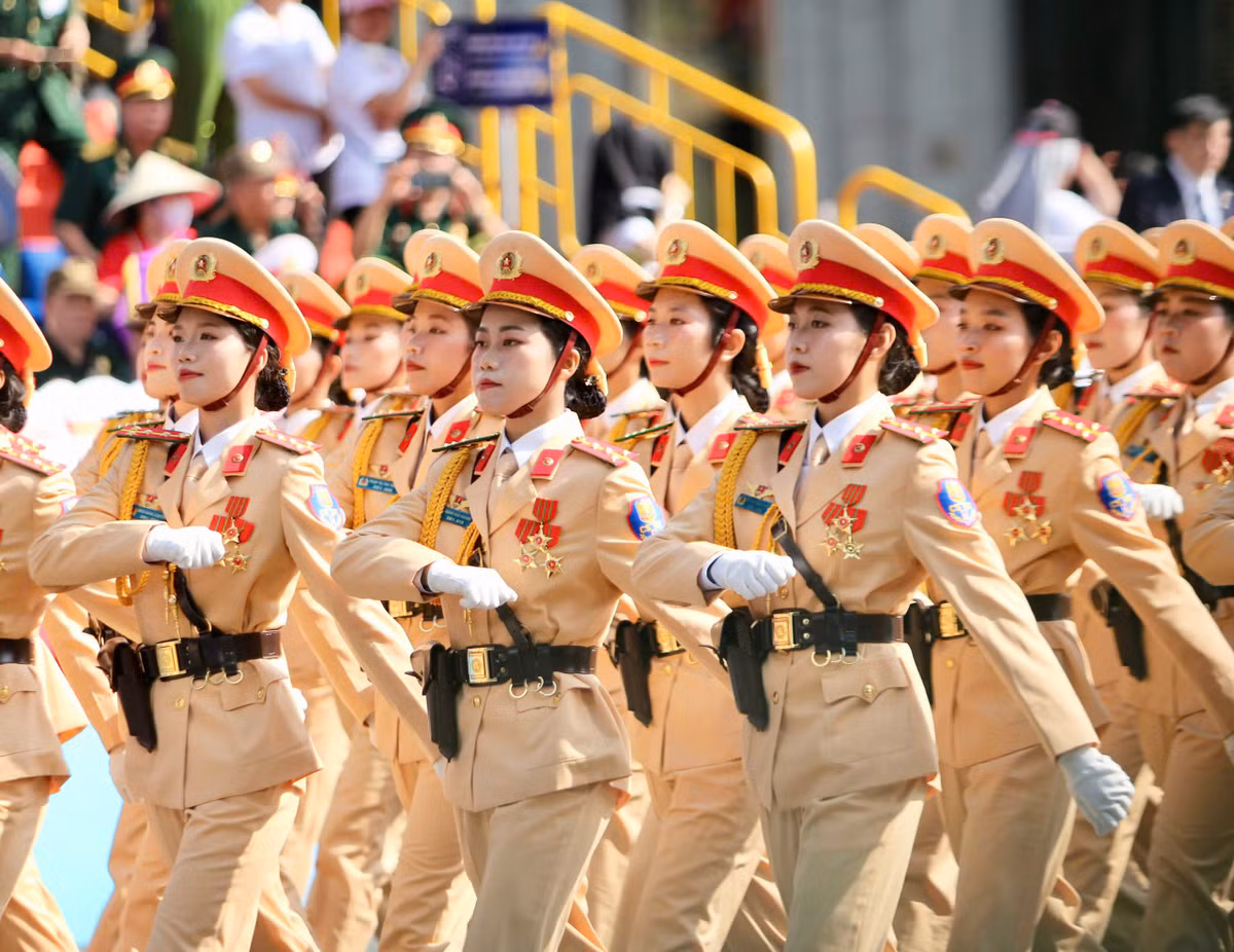 Khối nữ cảnh sát giao thông mặc lễ phục vàng kem đặc trưng, đội mũ kê-pi viền đỏ, mang găng tay trắng và thắt lưng da nâu, diễu hành trang nghiêm và đồng bộ.