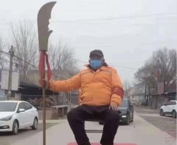 Một người đàn ông ở Vũ Hán, đeo khẩu trang, tay cầm đao ngồi nghiêm trang ngay chỗ cấm các phương tiện đi vào.