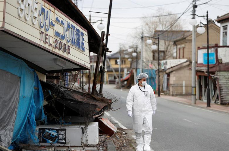 Yuji Onuma, một người di tản khỏi thị trấn Futaba, gần nhà máy điện hạt nhân Fukushima Daiichi - nơi bị tê liệt vì thảm họa động đất sóng thần 9 năm trước, mặc quần áo bảo hộ đi bộ qua một cửa hàng đổ sập trên phố ở Futaba, quận Fukushima, ngày 20/2/2020. (Nguồn ảnh: Reuters)