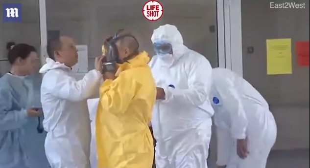 Một chuyên gia y tế đang giúp Tổng thống Putin mặc bộ quần áo và đeo kính bảo hộ khi vào thăm bệnh viện.