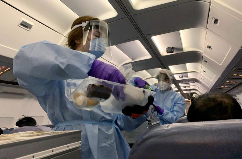 Tiếp viên hàng không mặc quần áo bảo hộ, đeo khẩu trang, phục vụ đồ ăn nhẹ cho hành khách Canada trên một chuyến bay chở họ đến Căn cứ Lực lượng Canada Trenton từ sân bay quốc tế Vancouver. Mời độc giả xem thêm video: Cách nhận biết người có biểu hiện nhiễm virus corona (Nguồn video: VTC1)