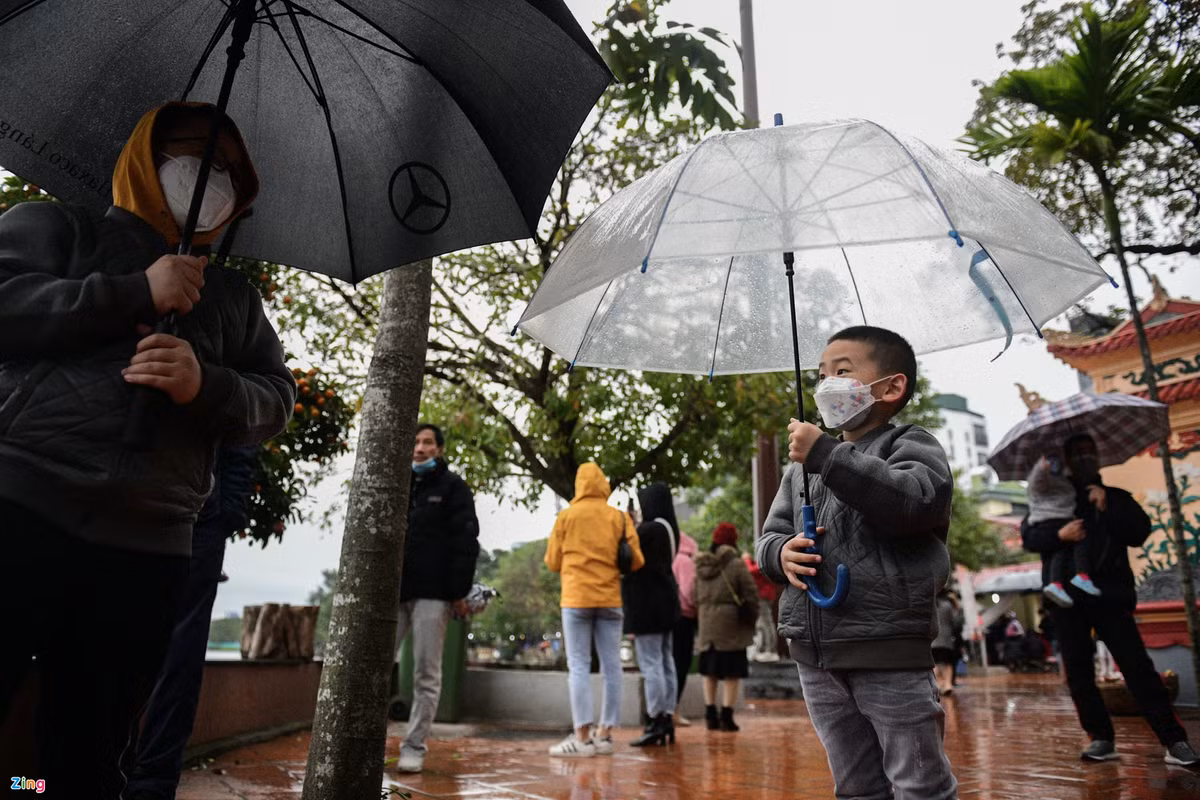 Trong chiều 13/2, Hà Nội mưa phùn, nhiệt độ giảm còn 13-14 độ C. Nhiều người phải mang theo ô, mũ khi đi lễ phủ.