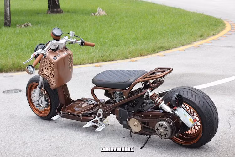 Bộ khung phụ phía trên của Zoomer đã được Dorbyworks chế lại, tạo thêm baga và chỗ bắt xi-nhan LED phía sau. Trong khi đó, pad biển số và đèn hậu được dời xuống cạnh bánh sau. Xưởng độ cũng đã sơn lại toàn bộ chiếc xe với màu đồng theo đúng phong cách steampunk.