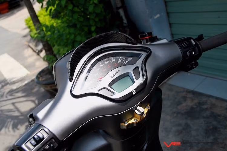 Ở phía trên khu vực tay lái, chiếc xe Vespa Sprint độ cũng được giữ nguyên cụm đồng hồ nguyên bản. Tuy nhiên bao xung quanh đồng hồ này là những điểm nhấn như "mào" chắn gió và viền ốp bằng sợi carbon của Zelioni. Nằm phía dưới cổ xe là cục trợ lực trung tâm Ohlins được gắn khéo léo, với nhựa cổ được khoét gọn gàng theo trợ lực.