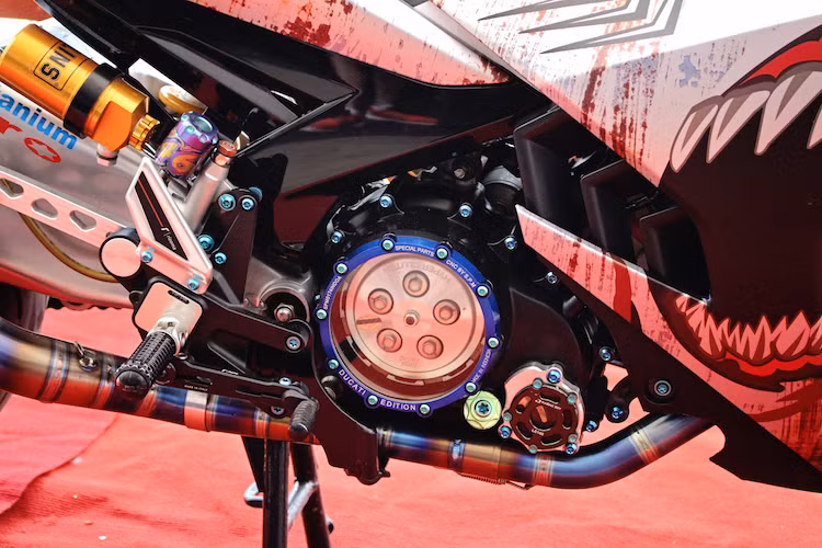 Khối động cơ nguyên bản của Exciter 135 đã được nâng công suất nhờ bộ lòng YCS trái 62 mm. Bưởng côn của chiếc xe được thay lốc trong suốt của S.P.M, lọc nhớt nắp CNC. Nắp mang cá chắn nhông là loại nhôm CNC của Rizoma. Chân chống bằng nhôm CNC cũng là một nét "chấm phá" độc đáo cho chiếc Exciter 135 độ này.