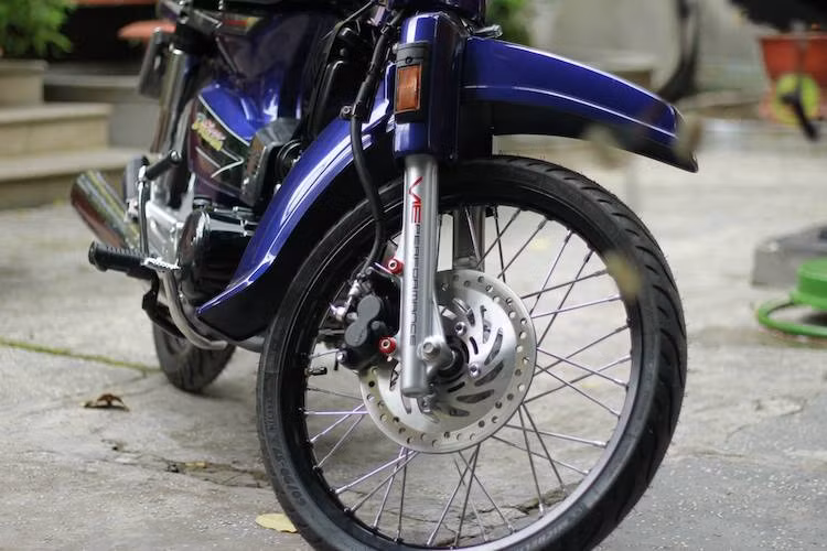 Ở phía trước, hệ thống phanh đùm nguyên bản đã được nâng cấp lên phanh đĩa 2 piston với đĩa từ Honda Wave RSX. Vốn đã chạy bánh căm ở dạng nguyên bản, tuy nhiên chiếc Super Dream Việt Nam này đã được thay cặp niềng nhôm màu đen nhẹ và sắc sảo hơn, đi kèm lốp Michelin Pilot Street bản mỏng.