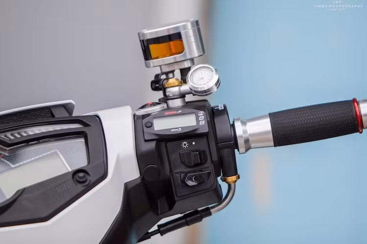 Khu vực tay lái cũng đã được chủ xe đầu tư nhiều món phụ kiện khác nhau, có thể kể tới như bình dầu Rizoma Next, bao tay Rizoma, cùm ga cuốn Domino và đồng hồ Koso Mini 3. Bảng đồng hồ Koso dành riêng cho Exciter 150 nằm thay vào vị trí đồng hồ "zin", với nhiều chức năng hơn.