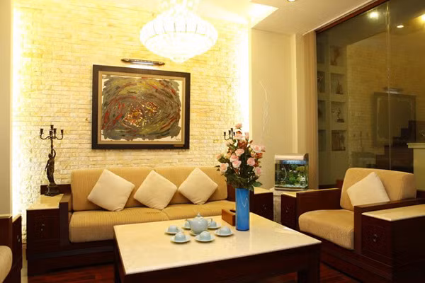 Phòng khách của nhà ca sĩ Hồ Quỳnh Hương được thiết kế xinh xắn, hiện đại với sofa gỗ. Toàn bộ phòng khách sử dụng màu kem làm chủ đạo, khi kết hợp cùng ánh đèn chùm vàng mang lại cho nơi đây không khí ấm áp, nhẹ nhàng, dễ chịu. Để tô điểm thêm cho không gian tiếp khách của mình, Hồ Quỳnh Hương treo tranh, đặt bể cá nhỏ và tượng.