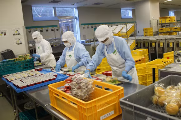 Nhân viên nhà máy sắp xếp thực phẩm đóng gói vào các khay và chuyển chúng lên xe đẩy đến phòng đông lạnh.