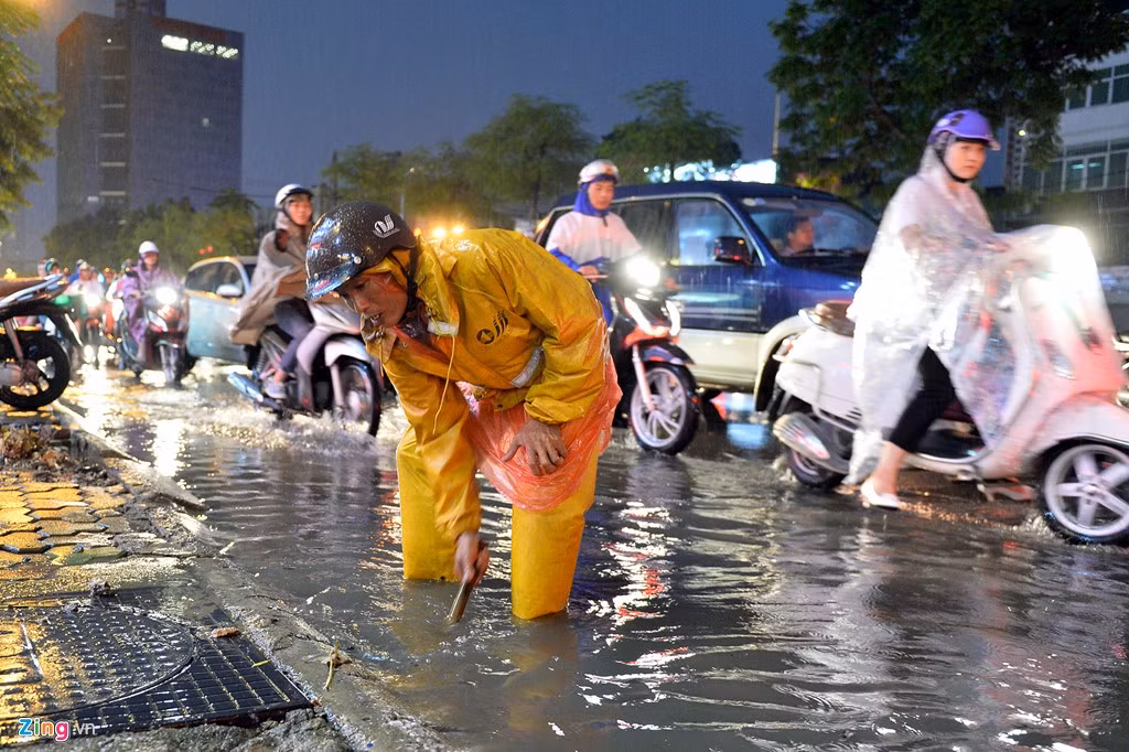 Nhân viên thoát nước cố gắng nhặt những mẩu vụn bị trôi vào chỗ khe nắp cống để nước rút nhanh hơn.