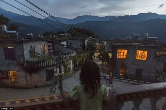 Xiao Yuan, 7 tuổi nhìn ra xa từ ban công nhà hàng xóm tại tỉnh Vân Nam. Em được sinh ra khi mẹ mới 17 tuổi. Yuan không được đi học dù đã quá tuổi quy định 1 năm.