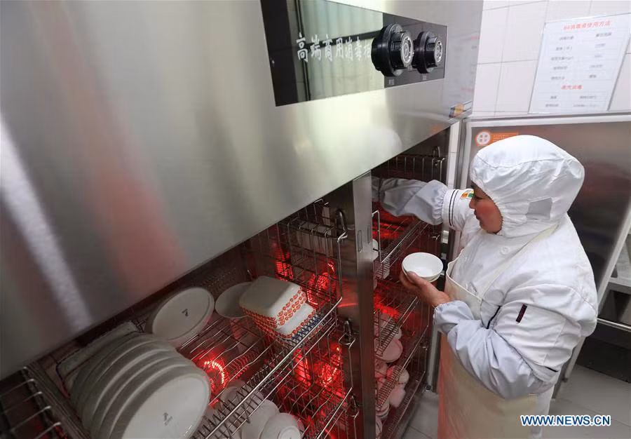 Một nhân viên đặt bát đĩa đựng suất ăn hàng không vào tủ khử trùng trong phòng ăn tại sân bay Nam Thông.