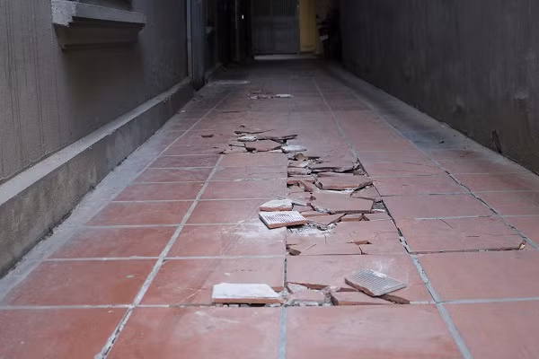 Sức nghiêng của ngôi nhà 4 tầng khiến nền đường gạch giữa hai nhà bị nứt, vỡ.