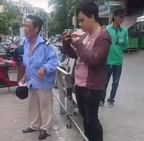 Sau khi đấm chảy máu miệng bảo vệ, nam thanh niên rút điện thoại ra bấm. Ảnh cắt từ clip.