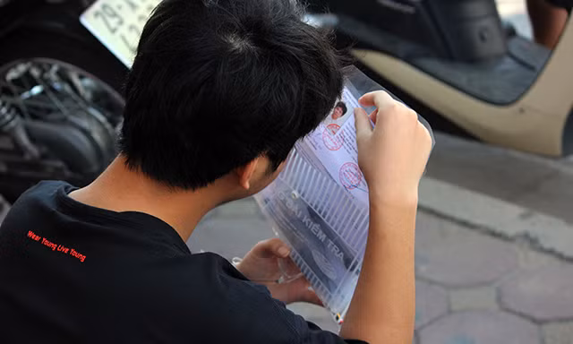 Một nam thí sinh đến điểm thi tuyển sinh lớp 10 từ sớm tranh thủ ngồi bên ngoài kiểm tra lại thẻ dự thi, cùng các giấy tờ liên quan trước khi vào làm thủ tục và nghe quy chế.