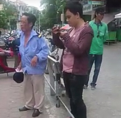 Sau khi đấm chảy máu miệng bảo vệ, nam thanh niên rút điện thoại ra bấm. Ảnh cắt từ clip.