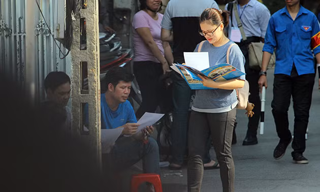 Cô gái cầm sấp tời rơi trên tay lần lượt phát cho các phụ huynh ở điểm thi trường THPT Yên Hòa (Hà Nội).