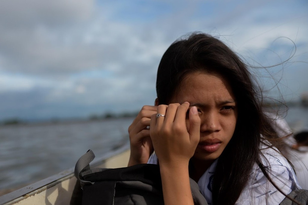 Danica che mặt cho khỏi nắng khi đi thuyền từ trường về nhà. Danica Martinez, 16 tuổi, lớn lên trong ngôi nhà phải nâng cao hơn cứ sau vài năm. Cha cô dựng cột chống cho túp lều tre của họ để nước từ biển không chảy xuống sàn. Họ sống ở Sitio Pariahan, ngôi làng ven biển ở Philippines từng là hòn đảo và hiện không có đất.