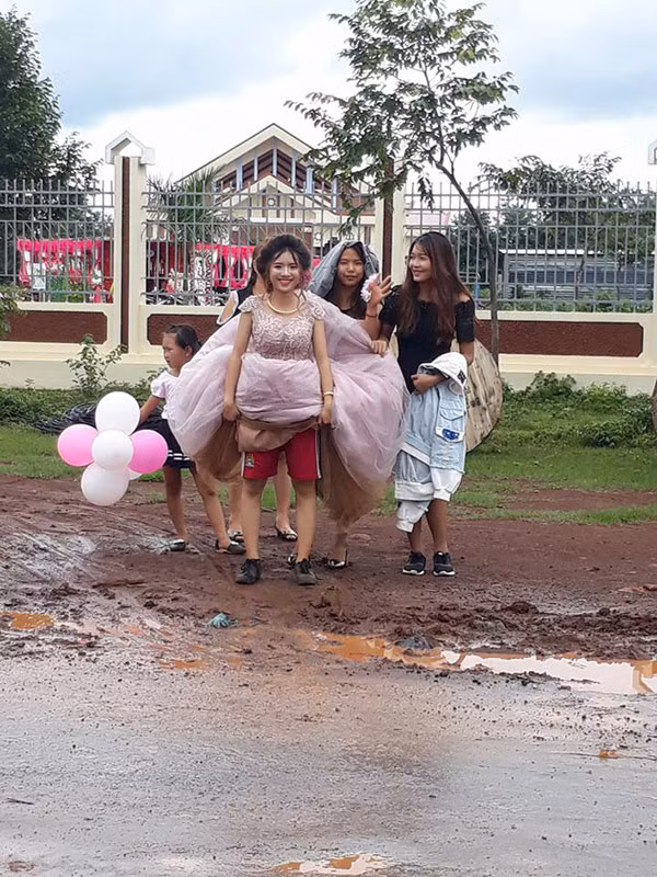 Đến khổ với mùa mưa là thế, ấy vậy mà cũng có lường trước được đâu. Nhất là những cô gái nào lỡ mang phận 'cô dâu' giữa mùa gió bão, đám cưới diễn ra ngay cái ngày mưa tuôn như trút, thì chỉ trong phút chốc, ngày vui lên xe hoa biến thành ngày Thủy Tinh giáng trần, muôn phần khổ ải. Nào là phải túm váy soire, vén quần áo dài, xách guốc lội bùn, che dù kẻo rơi mi giả… Cái chuyện đó, nỗi lo đó đã tái hiện y hệt trong một đám cưới tại vùng cao dưới đây khiến cô dâu váy áo lấm lem, mặt mày lem nhem mà vẫn phải nở nụ cười hiền, chuẩn kiểu 'hôm nay ngày vui của chị, mưa gió thế nào chị cũng phải ráng vui'. Mà hài hước nhất là cái cảnh khi cô dâu vén váy cưới thì bên dưới hiện nguyên hình y như một… cầu thủ bóng đá, với quần đùi và giày thể thao tất tả trong đám cưới ngày mưa.