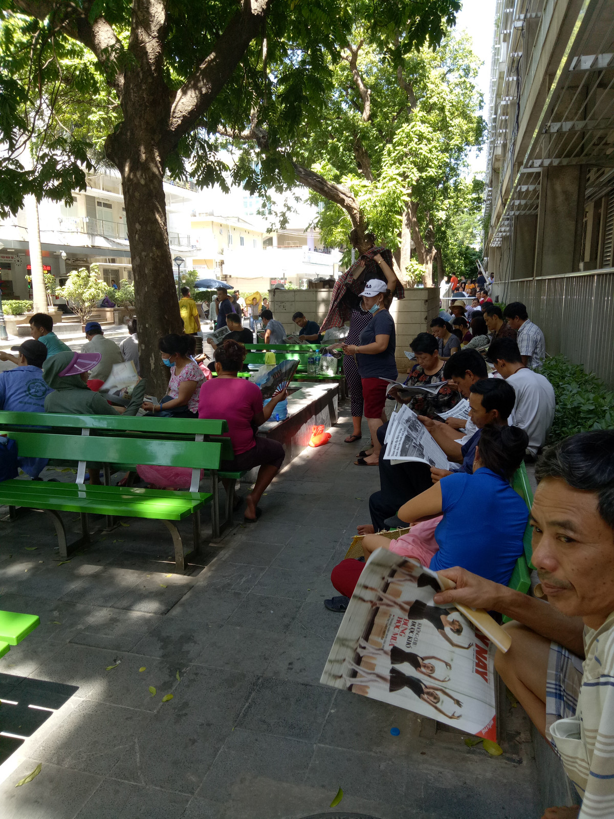 Ở khu ngoài trời, nhiều người nhà bệnh nhân mua tờ báo để vừa đọc, vừa là công cụ quạt mát.