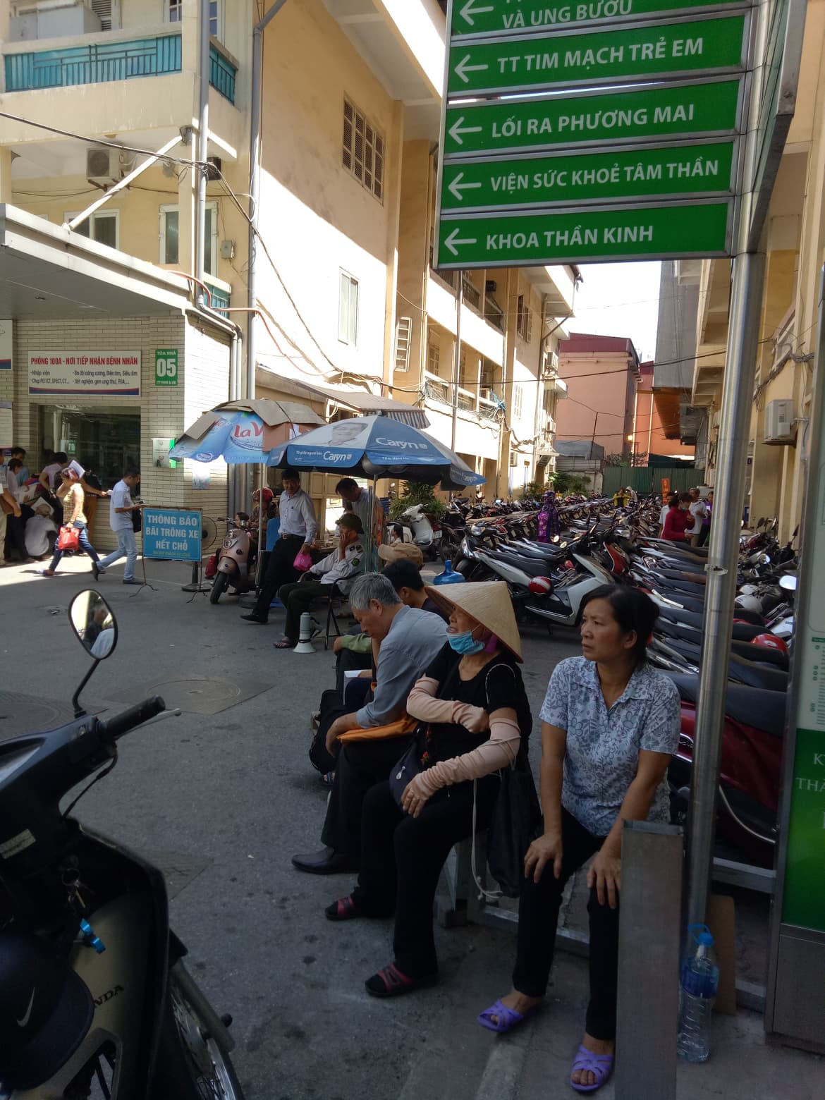 Một số bệnh nhân sang ngồi tận chỗ gửi xe, mệt mỏi chờ loa đọc đến lượt vì nơi này dẫu nóng nhưng không đông đúc, chen lấn.