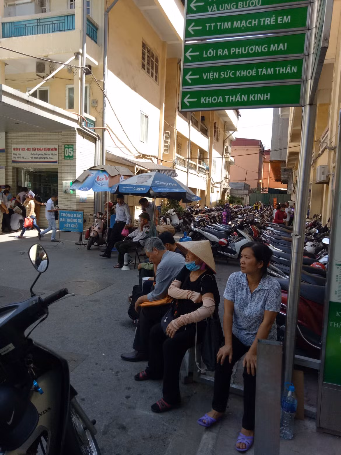 Một số bệnh nhân sang ngồi tận chỗ gửi xe, mệt mỏi chờ loa đọc đến lượt vì nơi này dẫu nóng nhưng không đông đúc, chen lấn.