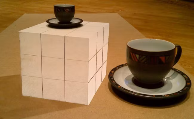 Một cái cốc đang nằm trên bàn, và cạnh cái cốc đó là một khối lập phương với một cốc nhỏ hơn trên nó. Tuy nhiên, nhìn từ một góc độ khác, bạn sẽ thấy lập phương là một bản vẽ và những chiếc chén có kích thước tương tự nhau. (Nguồn Brightside)
