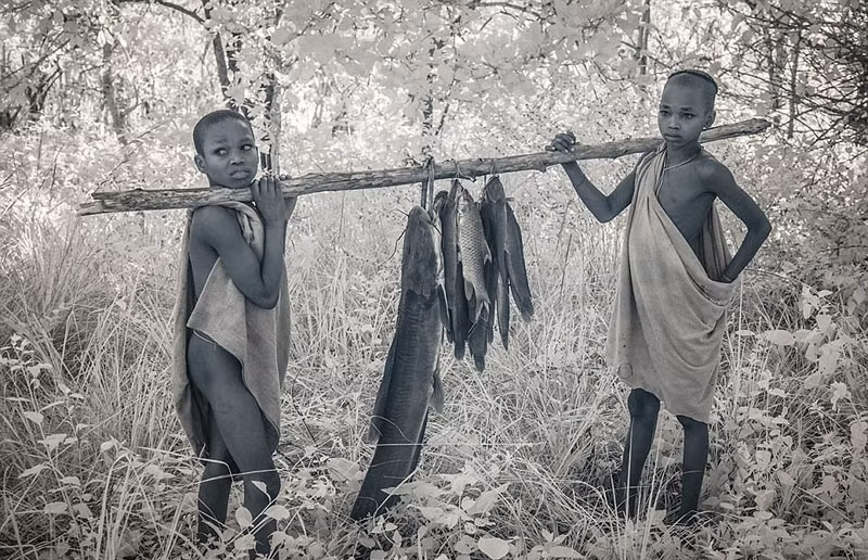 Trong lúc đó hai đứa trẻ khác chỉ quấn quanh mình tấm vải và khoe thành tích săn bắt cá của mình. (Nguồn Sina)