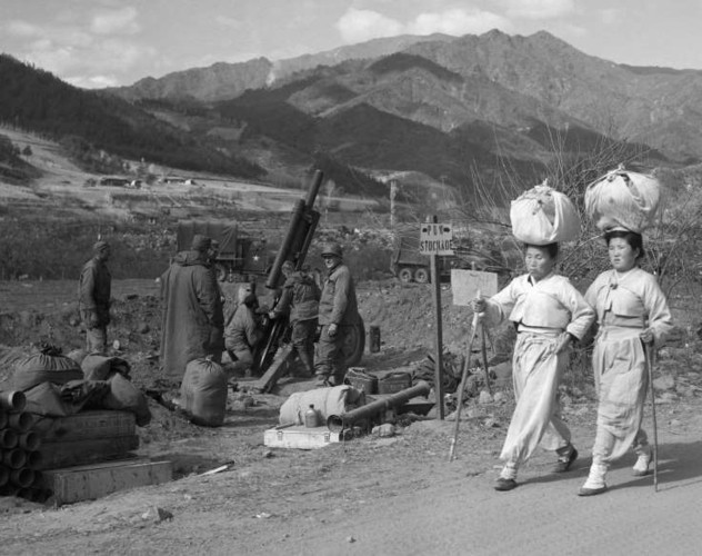 Những người phụ nữ Triều Tiên đi bộ qua một nhóm lính Thủy quân Lục chiến Mỹ đang chuẩn bị khai hỏa một quả pháo cối năm 1950.