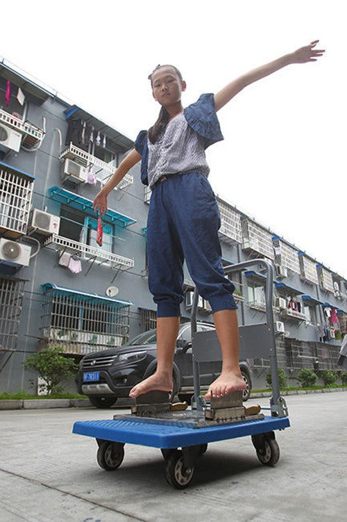 Không chỉ nhẹ nhàng đứng trên lưỡi dao mà cô bé "dị nhân" này còn tăng sự kịch tính bằng cách mỗi tay xách hai bình nước nặng 5kg để tăng sức nặng, tăng áp lực xuống đôi chân.