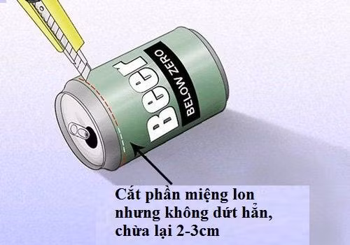 Cắt phần miệng lon nhưng cắt không hoàn toàn hết mà chừa lại gần phần lỗ khoảng 2 đến 3 cm. (Không để đứt mặt lon, tức phần miệng lon vẫn dính với thân lon)