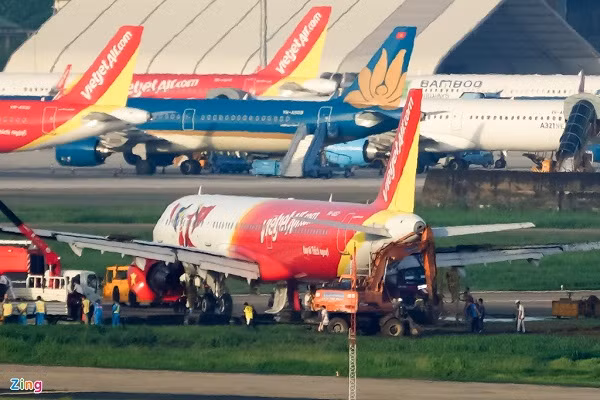 Xe lai dắt kéo tàu bay ra khỏi bãi bùn lầy, trong khi một xe cần cẩu hỗ trợ từ phía sau để chiếc A321neo không bị tụt lại.