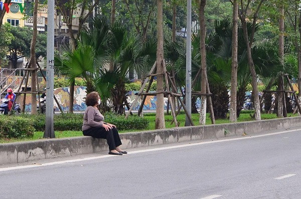 Một người cao tuổi ngồi nghỉ ngay bên đường sau khi tập thể dục.