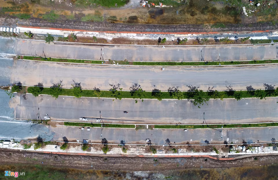 Theo khảo sát của Zing, sau 5 năm đầu tư, 4 con đường trong đô thị mới Thủ Thiêm hiện bị chậm tiến độ khi một số hạng mục vẫn ngổn ngang. Chủ đầu tư đang ngừng thi công vì chưa có mặt bằng. Cụ thể, tuyến đường R1 có mặt cắt ngang 55 m, 6 làn xe. Tại các phần đã thi công xong, đơn vị đầu tư đã cho trồng cây, lắp hệ thống chiếu sáng... Ảnh: Zing.