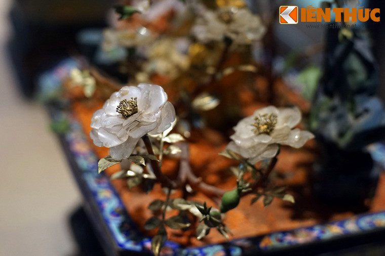 Xung quanh thân cây mai có nhiều loại hoa cỏ làm nền, nổi bật là một cây hoa hồng bạch với những cánh hoa làm từ đá trắng. Ngoài ra, còn có hai hòn giả sơn nhỏ bằng đá màu xanh phối ở hai góc.