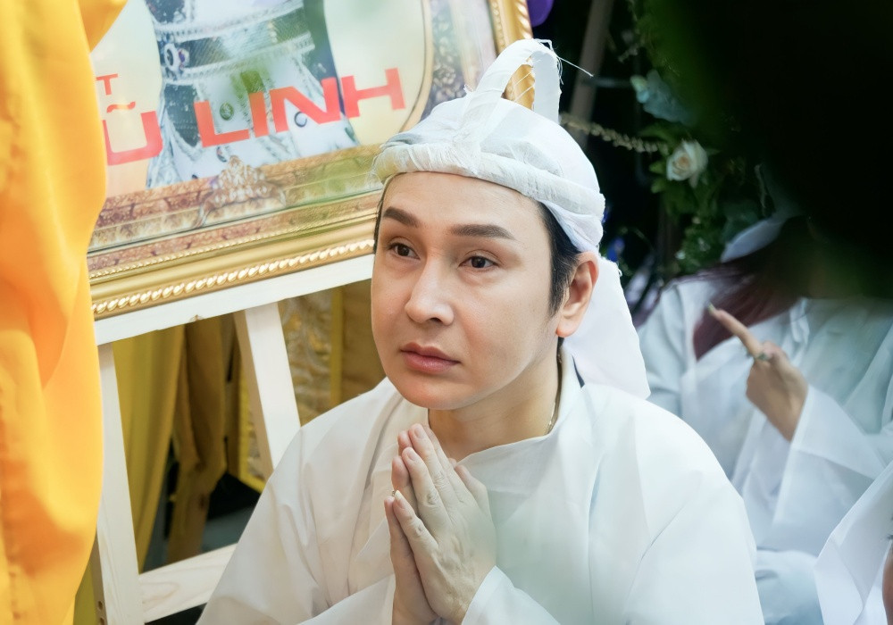 Vũ Luân bái lạy trước linh cữu cha nuôi. Anh tạm ngưng công việc từ lúc Vũ Linh đổ bệnh nặng để dành trọn thời gian bên ông.