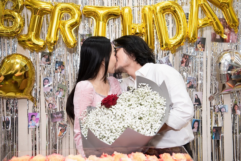 Đặc biệt, đạo diễn Hoàng Nhật Nam xuất hiện đầy bất ngờ khiến nữ CEO không khỏi ngạc nhiên và xúc động. Trong tay đạo diễn cầm bó hoa trắng, điểm xuyết giữa là bông hoa hồng đỏ, mang ý nghĩa “chỉ yêu mình em”. Vợ chồng "bà trùm hoa hậu" đã dành cho nhau một nụ hôn nồng cháy.