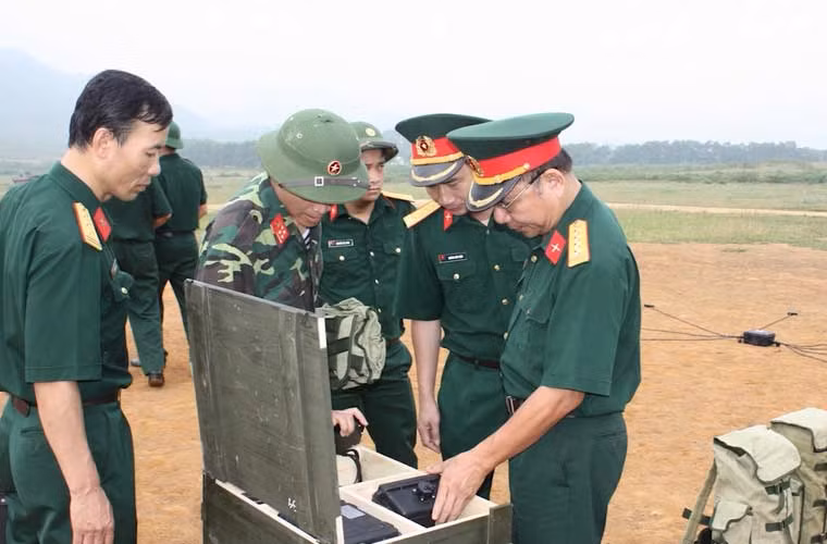 Trước đây, trong diễn tập, các đơn vị quân đội thường làm bãi tạo giả rất thủ công, như: Cắt dây cháy chậm với độ dài khác nhau; gây nổ bằng nụ xòe hoặc đốt bằng bùi nhùi. Sau này, nhờ ứng dụng các tiến bộ kỹ thuật, các cán bộ đã dùng kíp điện để điều khiển nổ thông qua bộ điều khiển bằng các thiết bị, linh kiện điện tử. Ảnh: Triển khai làm bãi tạo giả và bố trí các thiết bị điều khiển nổ.