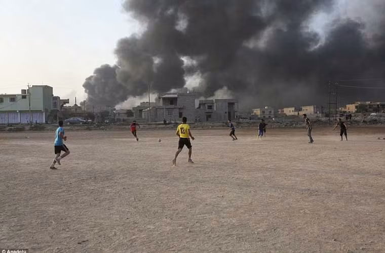 Lũ trẻ chơi đá bóng khi các đám khói bốc lên ngùn ngụt.