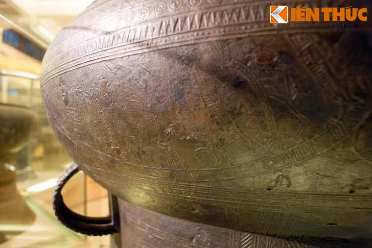 Phần dưới tang trống là 6 chiếc thuyền chuyển động từ trái sang phải, chở chiến binh tay cầm vũ khí và tù binh, xen giữa là những hình chim cò ngậm cá, chó săn được thể hiện theo lối cách điệu.