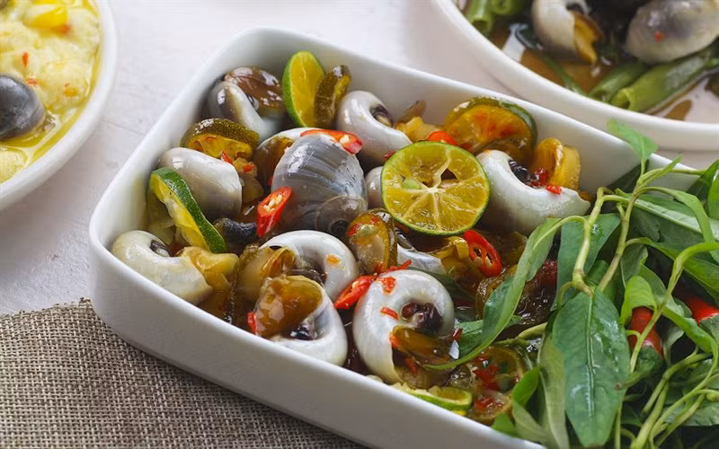 Cách làm: Đun một nồi nước thật sôi, thêm vào 15gr gừng cắt lát đập dập, cho ốc vào trụng sơ 2 phút sau đó vớt ra rửa sạch. Vắt lấy nước của 6 trái tắc, cho nước tắc vào nồi cùng với 4 muỗng canh đường và 2 muỗng canh nước mắm. Khuấy đều cho hòa quyện.